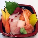 Chirashi sushi bowl featuring assorted sashimi cuts including salmon, tuna, shrimp, octopus, and imitation crab, garnished with wasabi, pickled radish, and shiso leaf in a lacquered bento box