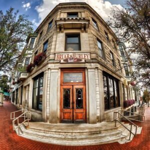 Storefront of The Briar & Burley, a historic-looking building with a prominent wooden door, large windows, and flower arrangements, photographed by Kendall Reeves.