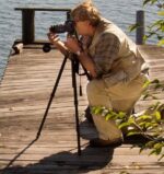 Tom Duffy composes a shot with a tripod-mounted camera while working from a wooden dock by the water. Tom Duffy composes a shot with a tripod-mounted camera while working from a wooden dock by the water.