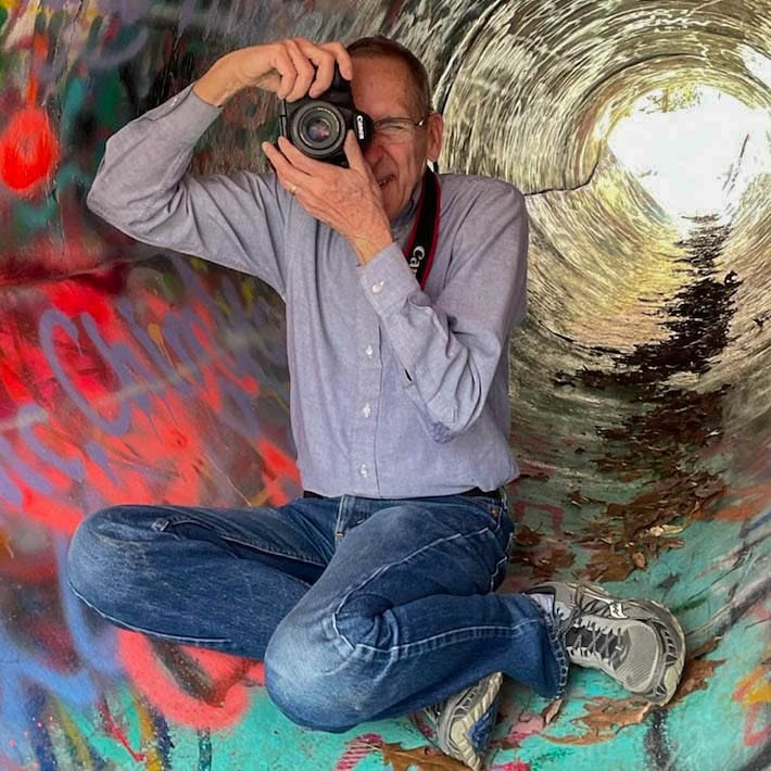 Dale Staton photographing with a camera in front of colorful abstract artwork
