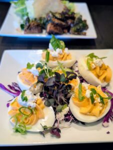 Five deviled eggs with orange filling, garnished with crumbled white cheese and green onions, served over microgreens and red cabbage.