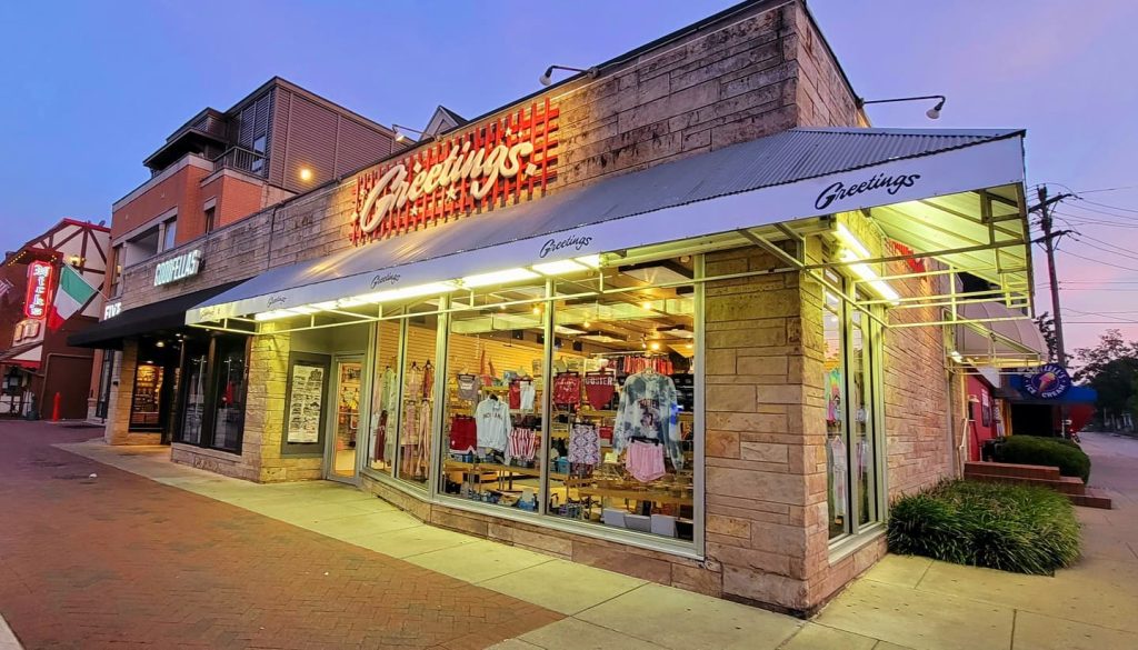 Evening view of Greetings Gift Shop on Kirkwood Avenue in Bloomington, Indiana, with bright storefront lights and merchandise displayed in the windows