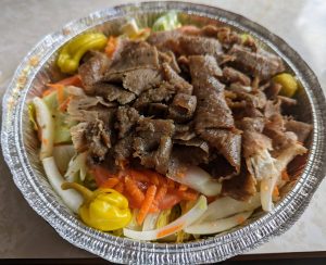 Gyro salad from King Gyros in Bloomington, featuring shaved lamb gyro meat over fresh lettuce, carrots, onions, tomato slices, and banana peppers in a foil container.