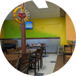 Interior of Los Potrillos Tex-Mex & American Restaurant in Solsberry, Indiana, featuring wooden chairs and tables, yellow-green walls, a red sun wall decor, and a casual dining atmosphere