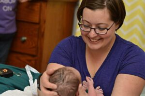 A midwife smiling as she holds a newborn during a postpartum visit
