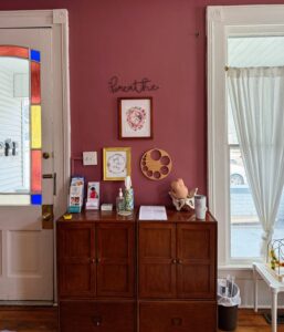 The welcome area inside the Mother Nurtured Midwifery office, with a red wall, stained glass and a small display of handouts