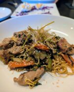 A steaming bowl of savory stir-fried noodles tossed with crisp vegetables and tender cuts of meat.