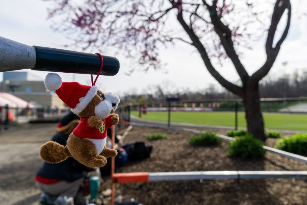 A small plush mascot wearing a festive hat hangs from a bicycle repair stand at the track.