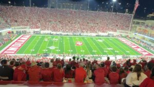 Indiana University Memorial Stadium at night, packed with fans in red, with the field lit under the stadium lights